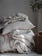 Leinen Bettwaesche Set in Beige und Weiss, gestapelte Kissen und Decken auf Sessel