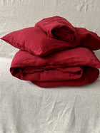 Leinen Bettwaesche Set in Karminrot, gestapelte Kissen und Decken auf hellem Teppich