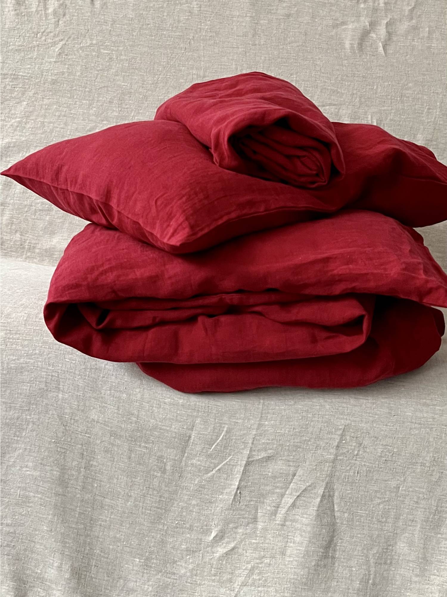 Leinen Bettwaesche Set in Karminrot, gestapelte Kissen und Decken auf hellem Teppich